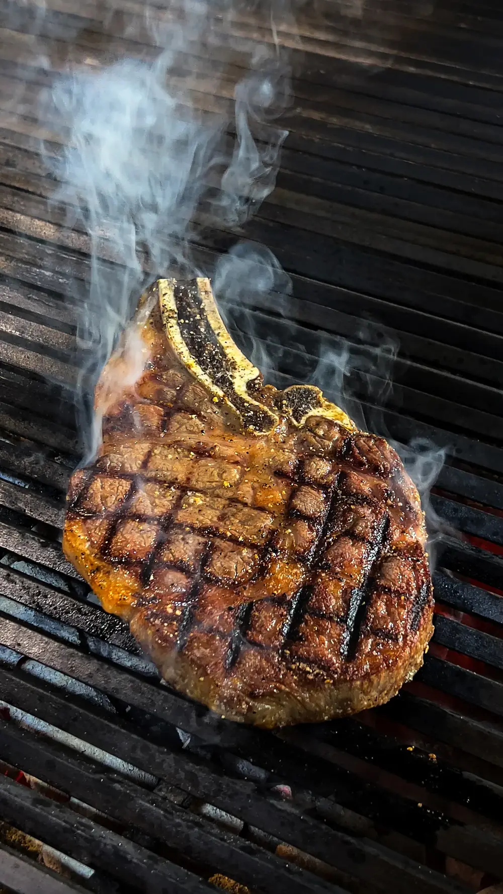 A perfectly grilled T-bone steak with crosshatch marks on a smoky barbecue