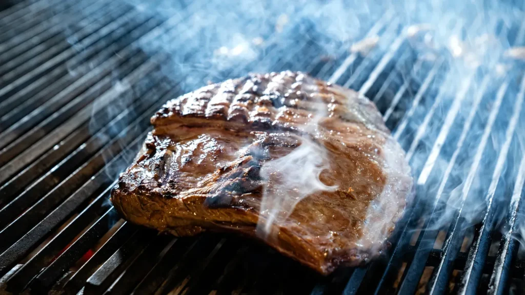 Meat cooking temperature chart: steaks sizzling with smoke on a grill
