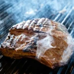 Meat cooking temperature chart: steaks sizzling with smoke on a grill