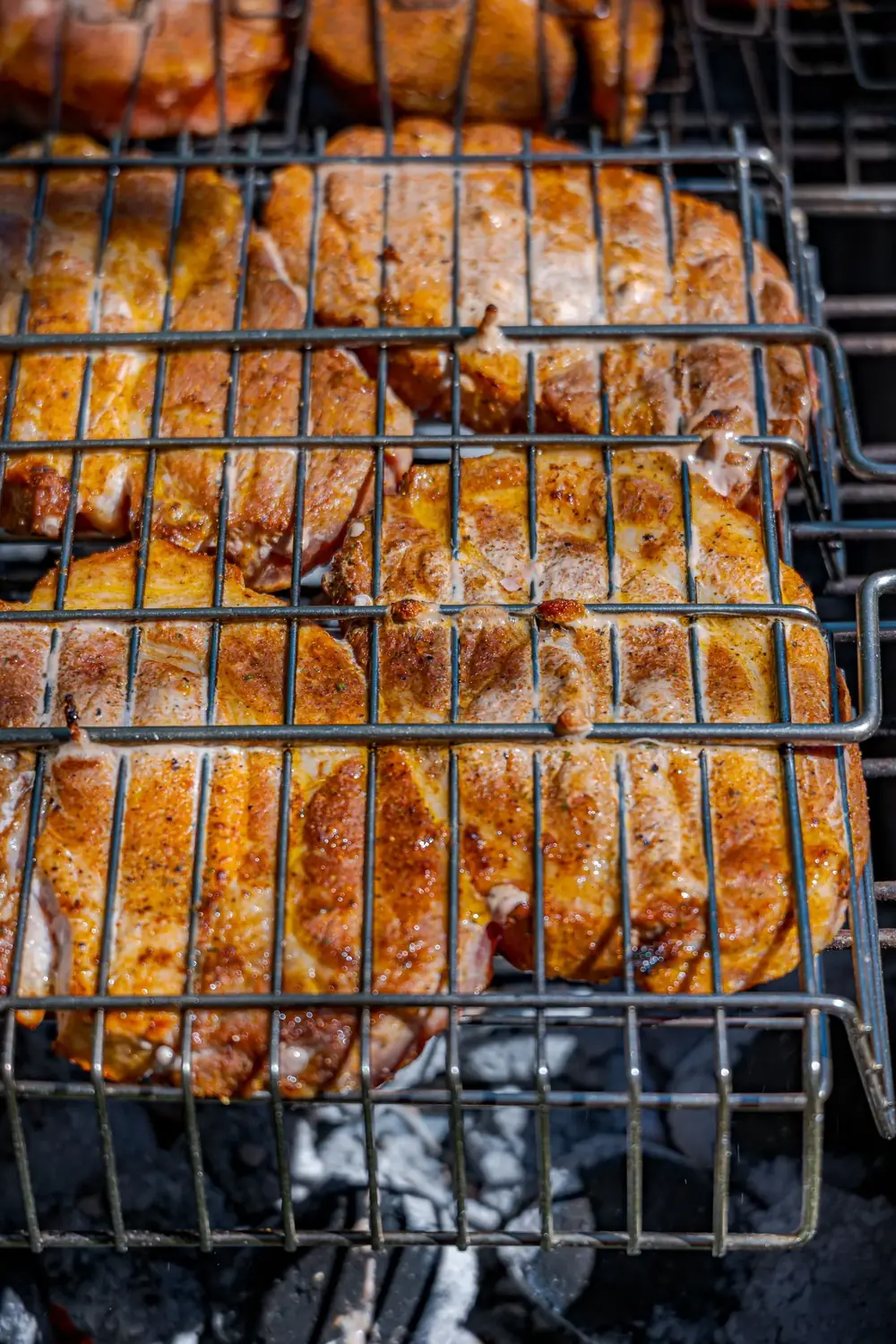 Seasoned pork chops grilling over charcoal in a grill basket
